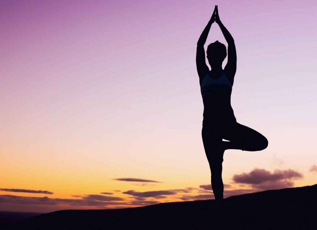 Silhouette of woman practicing yoga at sunset